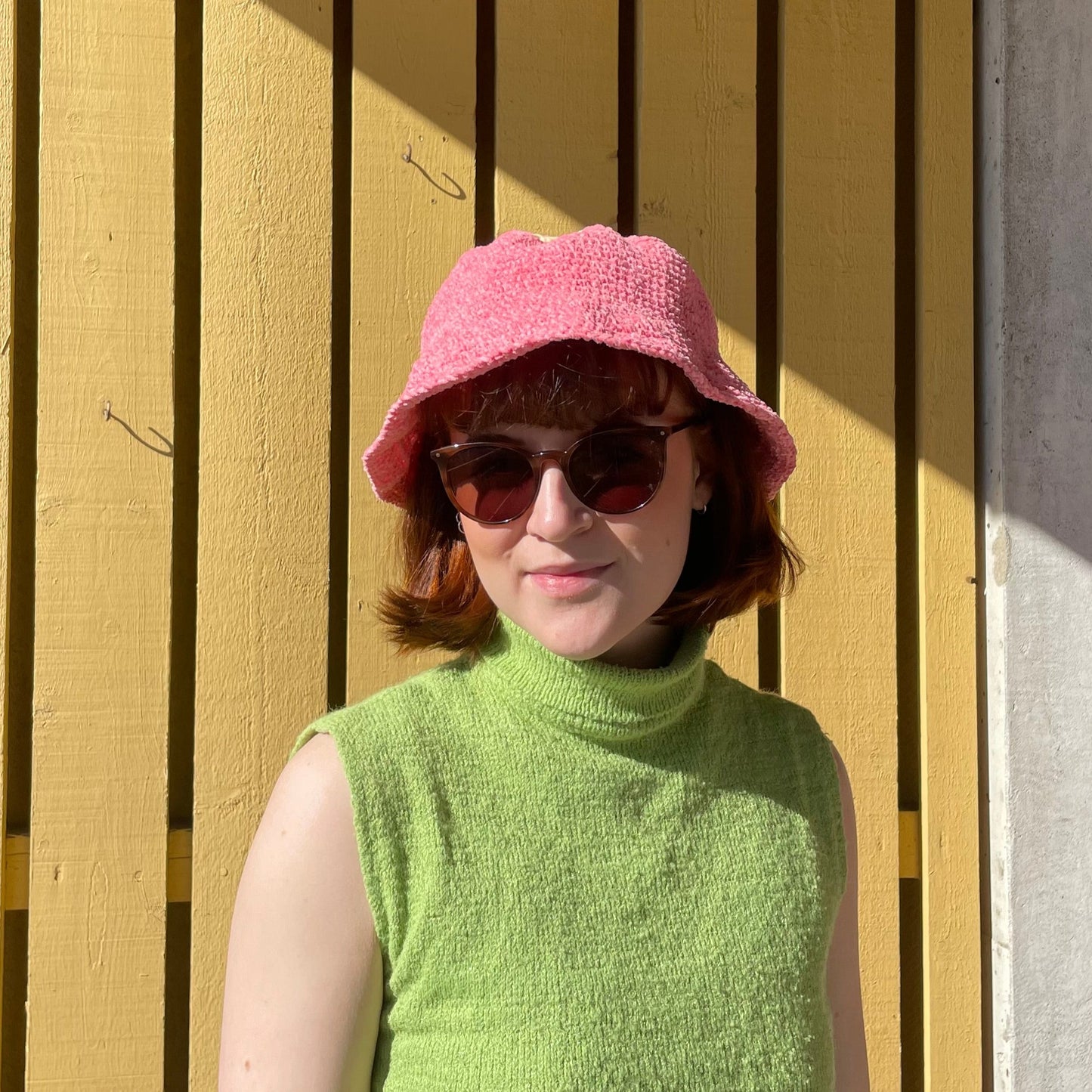 Rosa bucket hat som bärs i solen på en balkong, perfekt för att både skydda mot solen och liva upp en sommaroutfit.