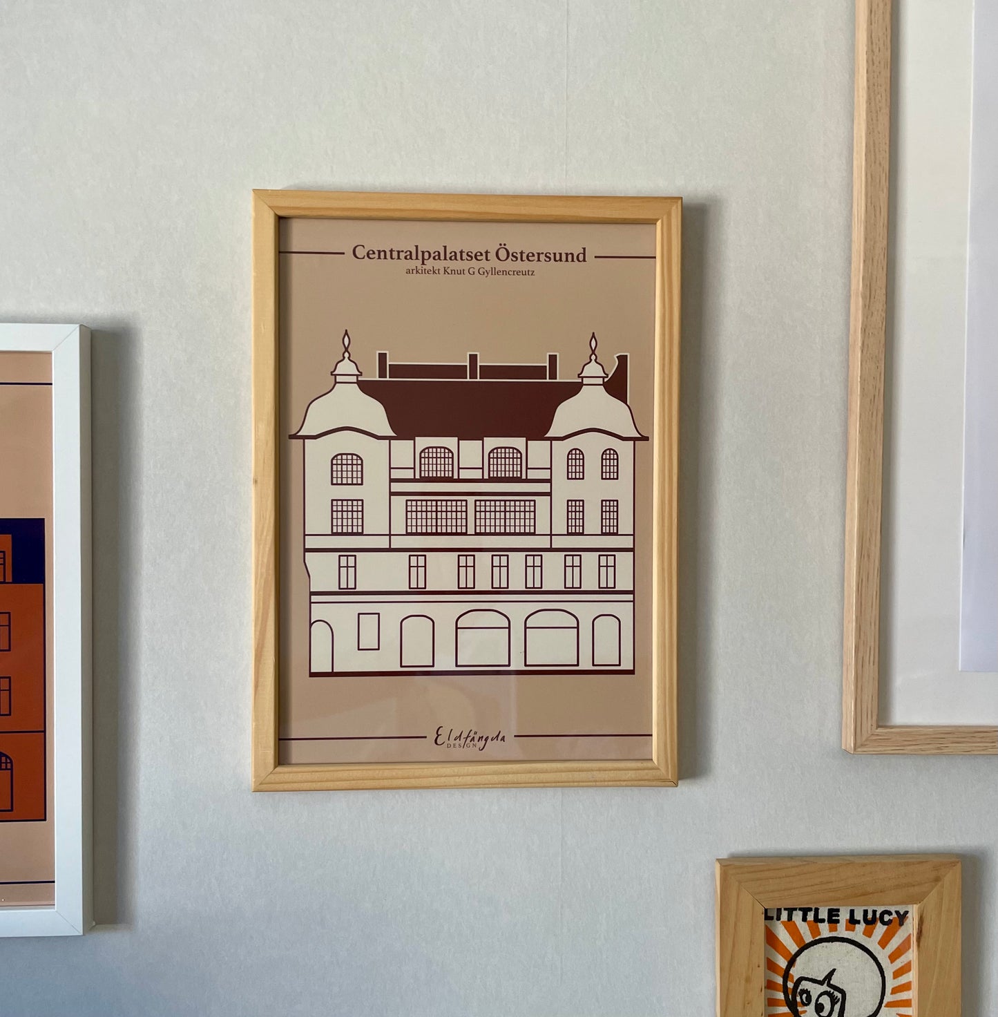 En inramad poster som hänger på väggen. Postern har ett illustrerat motiv av det gamla centralpalatset i Östersund.